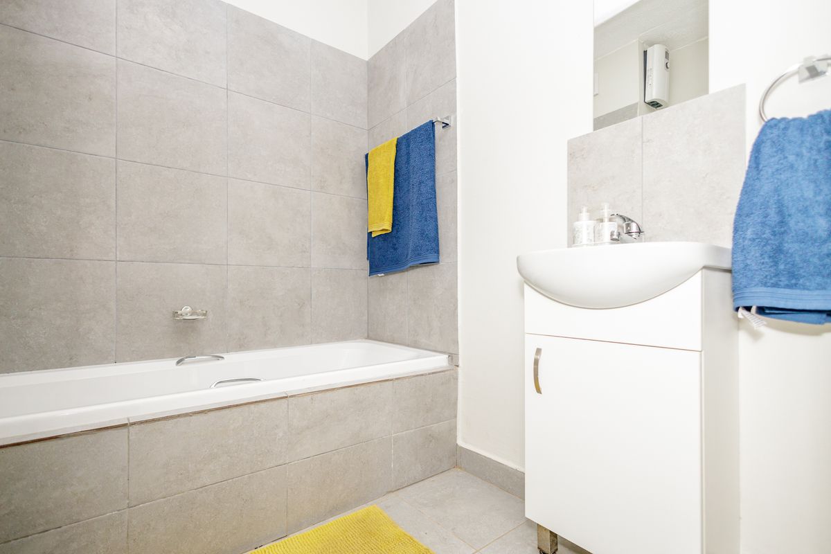 A clean, modern bathroom featuring a built-in bathtub with grey wall tiling and a white vanity cabinet with a basin.