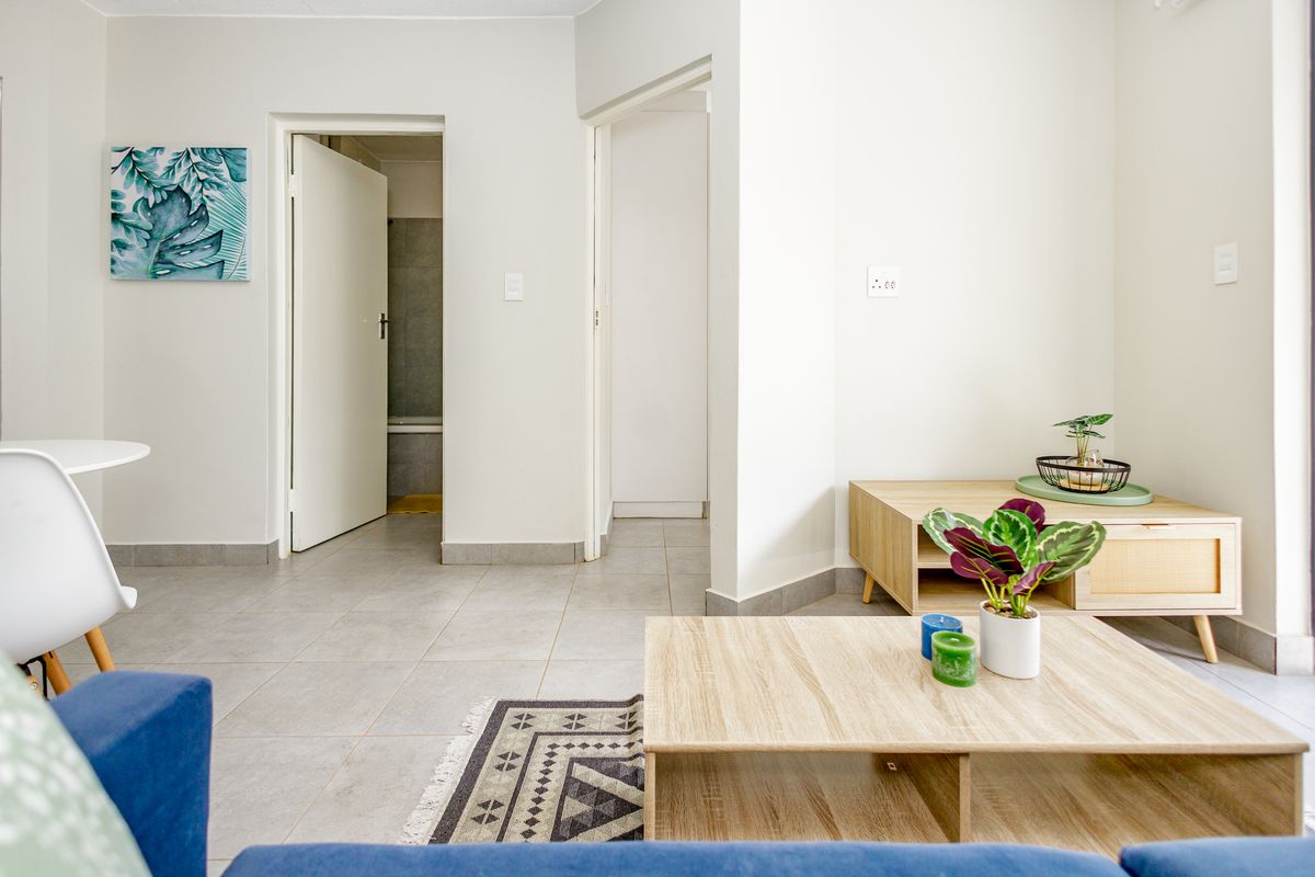A bright, open-plan living area featuring neutral tiled flooring and clean white walls, providing a versatile space with access to adjacent rooms.