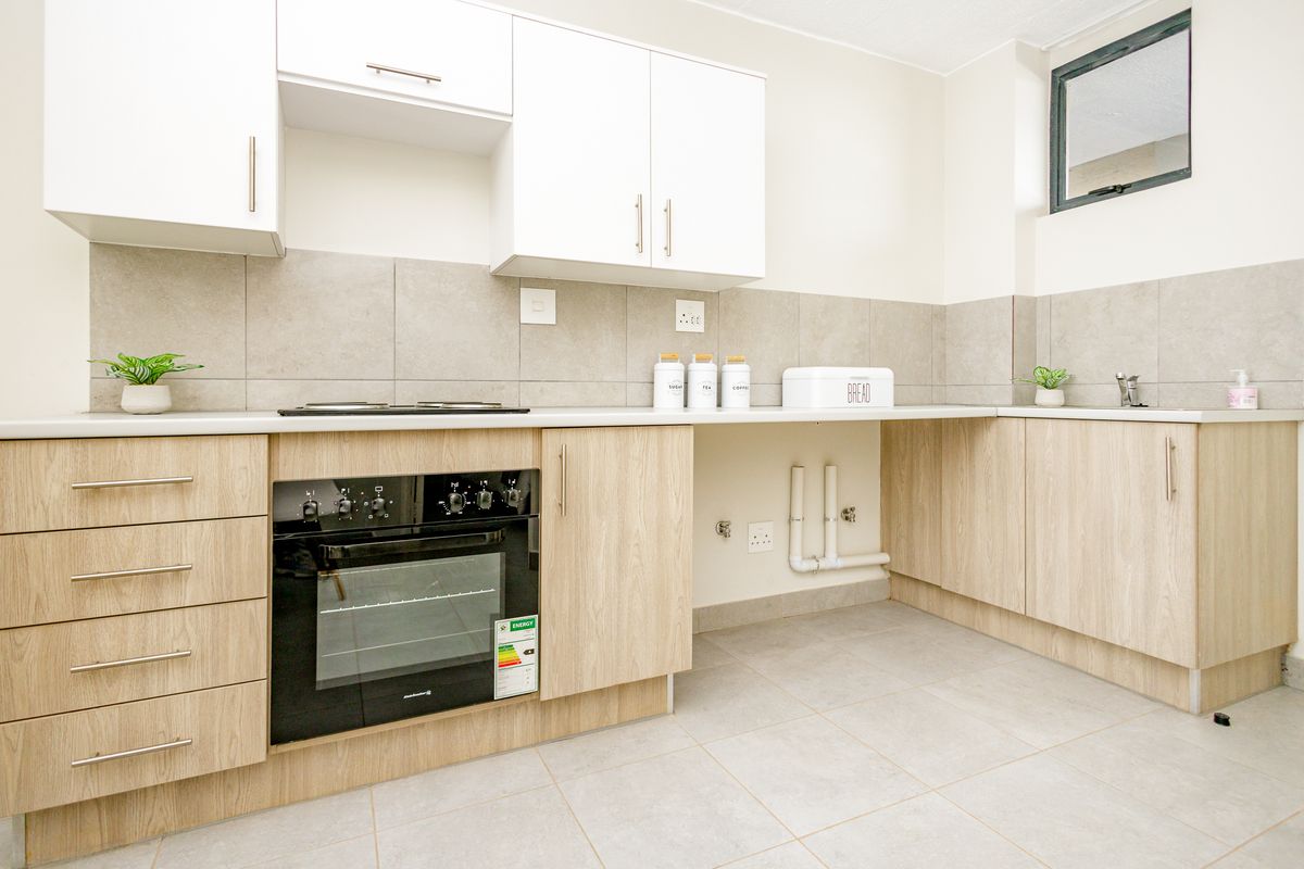 Modern kitchen featuring light wood-finish cabinetry, built-in oven, hob, neutral tiled backsplash, and dedicated plumbing connections for appliances.