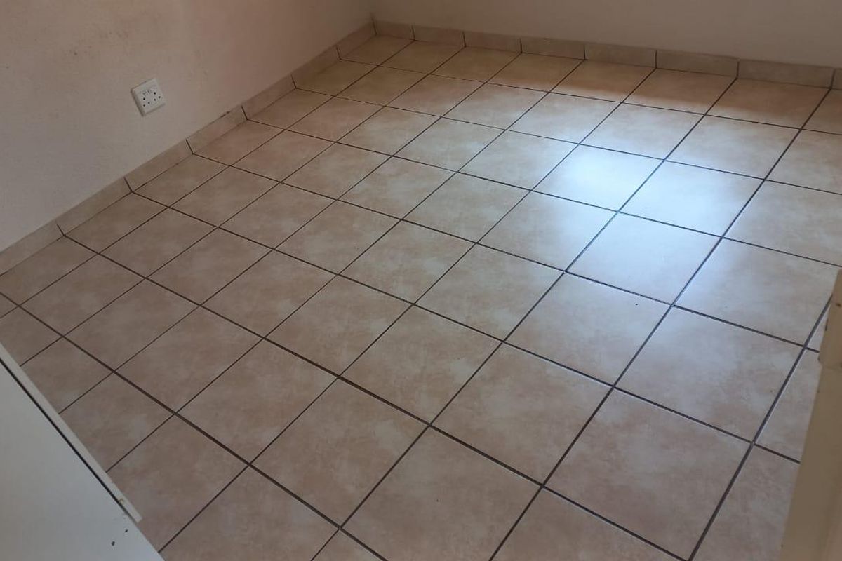A vacant bedroom featuring neutral ceramic floor tiles and a standard electrical wall outlet.