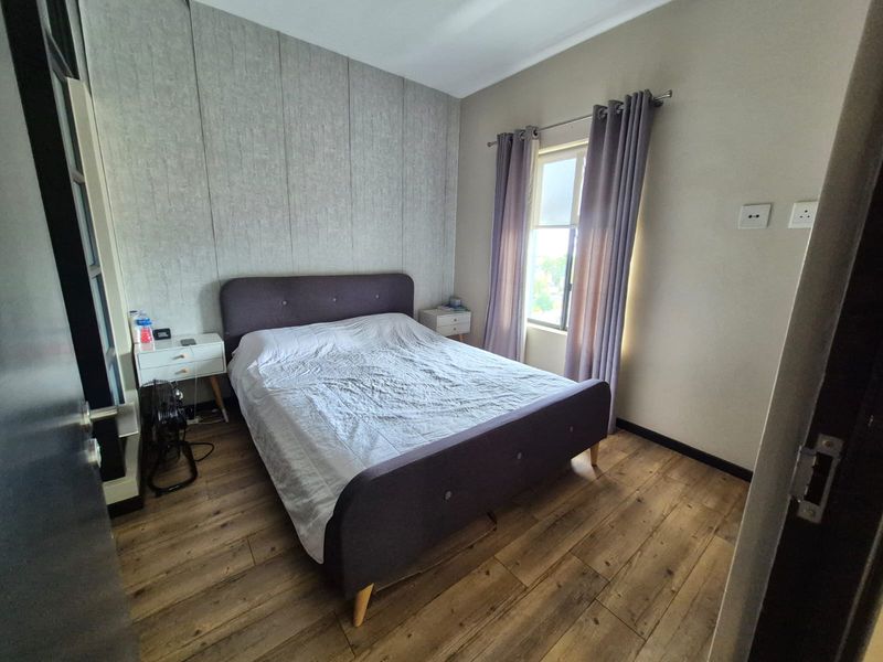 A well-maintained bedroom featuring wood-look laminate flooring, a textured feature wall, and natural light from a side window.