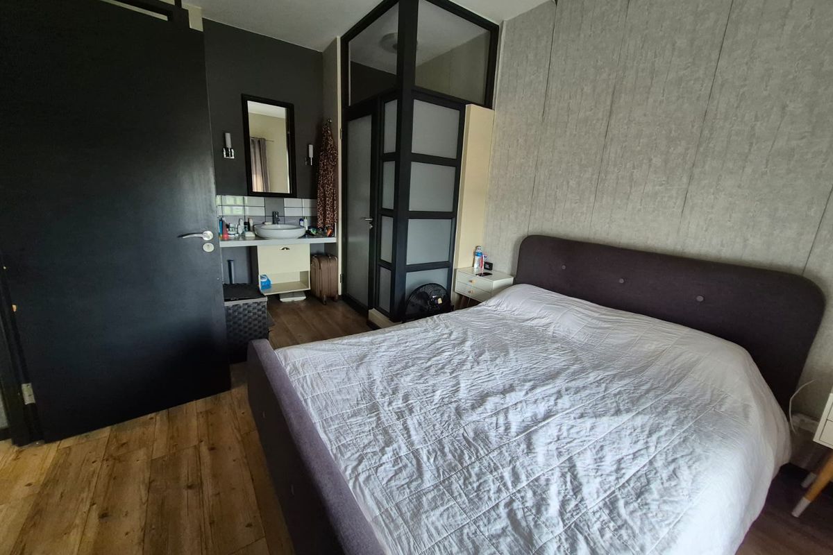 Bedroom featuring integrated vanity basin, frosted glass partition, textured wallpaper, and laminate flooring.