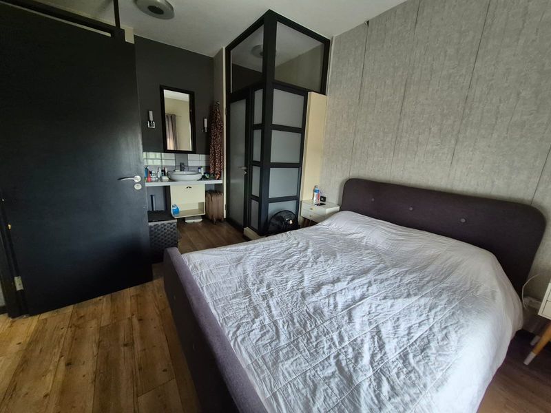 Bedroom featuring integrated vanity basin, frosted glass partition, textured wallpaper, and laminate flooring.