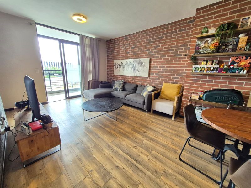 Spacious living room featuring an exposed brick feature wall, laminate flooring, and large sliding glass doors leading to a balcony.