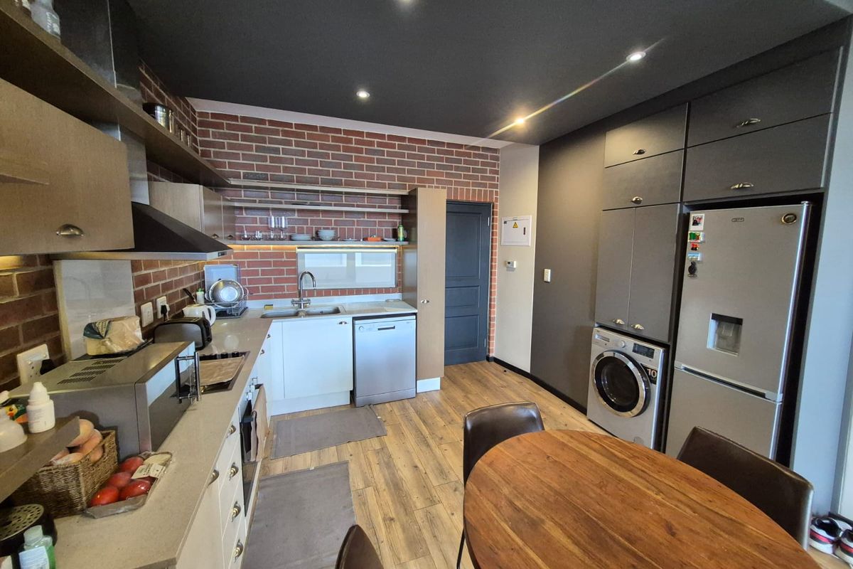 Modern open-plan kitchen featuring exposed brick accents, sleek cabinetry, integrated appliances, and recessed lighting, creating a functional and stylish living space.