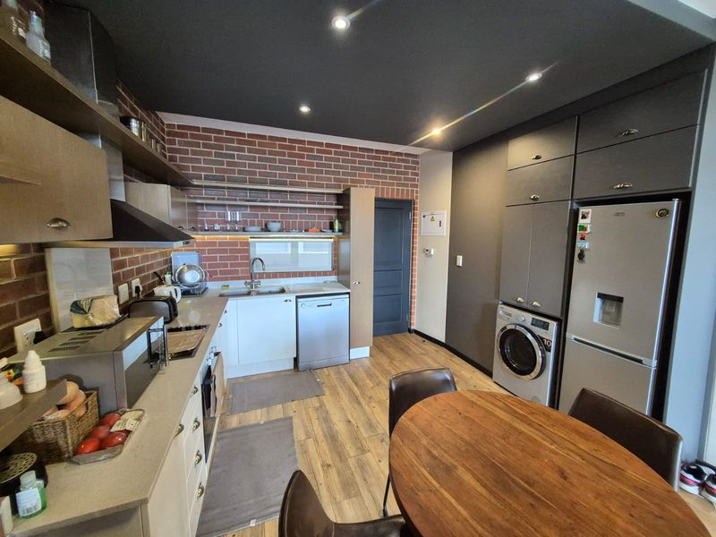 Modern open-plan kitchen featuring exposed brick accents, sleek cabinetry, integrated appliances, and recessed lighting, creating a functional and stylish living space.