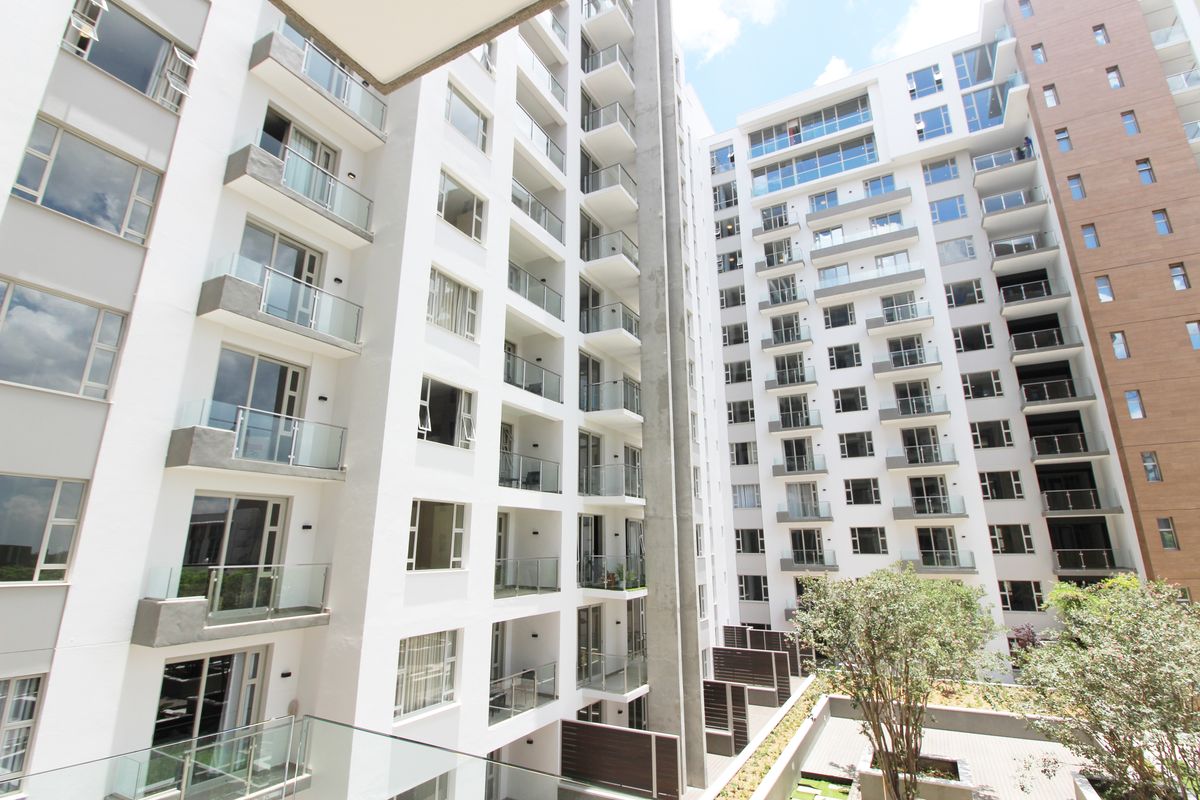 A view of the modern apartment complex exterior, featuring multiple levels of balconies with glass balustrades and a landscaped courtyard area below.
