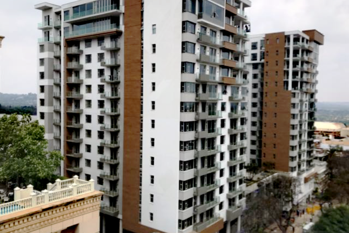 Aerial view of a modern multi-story apartment complex featuring contemporary architectural design, glass balconies, and a mix of white and wood-tone facade finishes.
