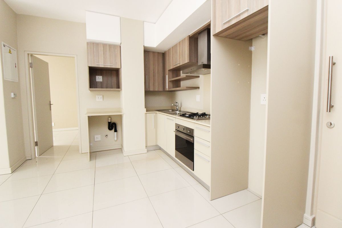 A modern, empty kitchen featuring built-in cabinetry, a gas hob, an electric oven, and tiled flooring, ready for immediate use.