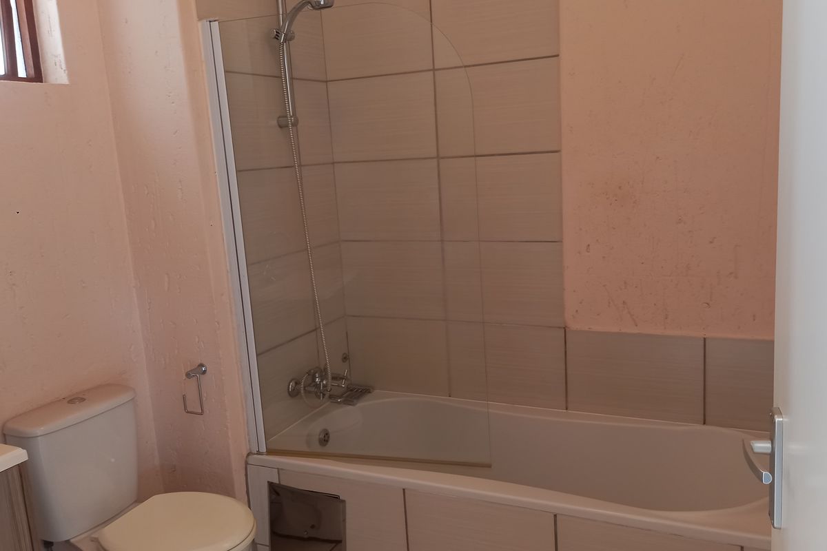 A functional bathroom featuring a bathtub with a glass shower screen, a toilet, and tiled splashback areas.