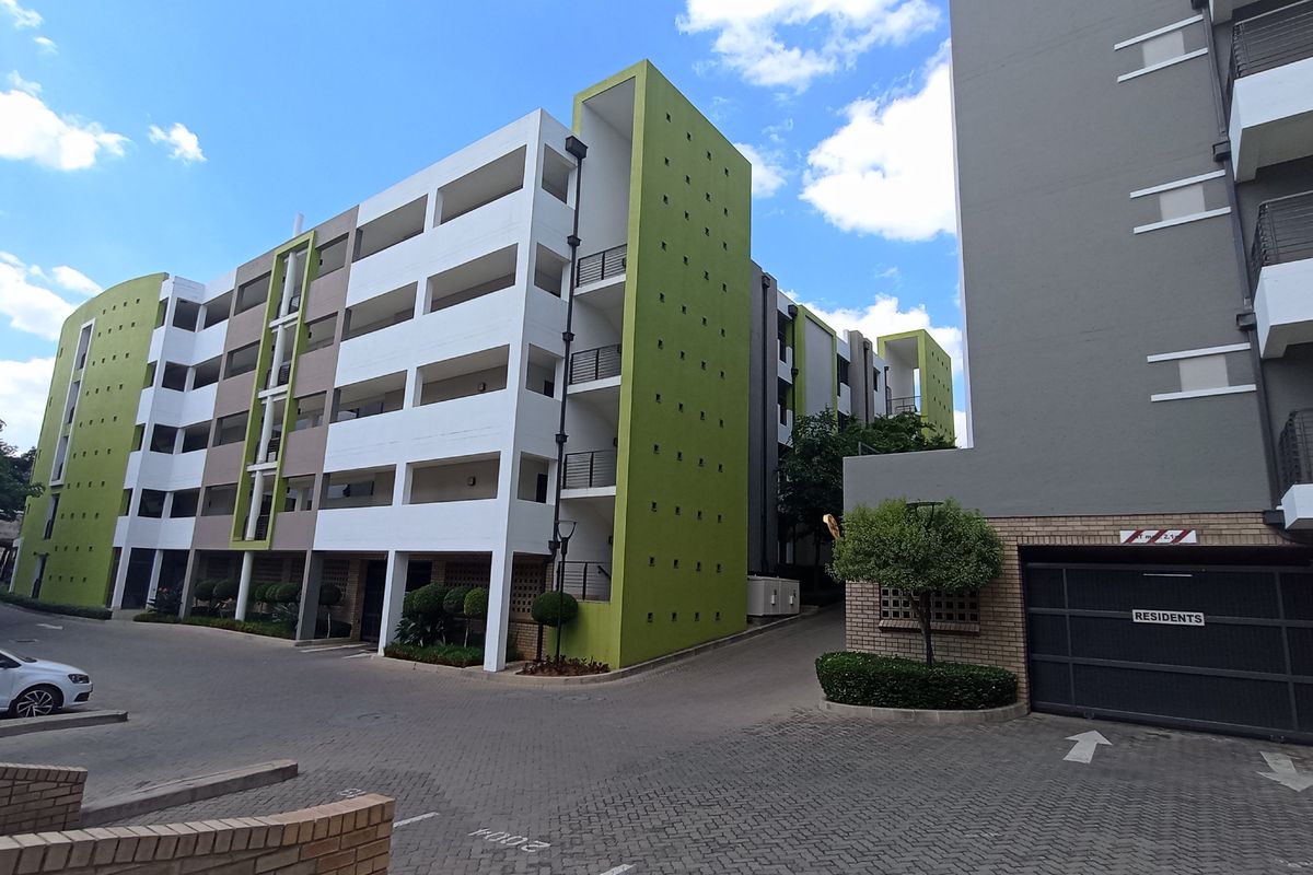 Exterior view of a modern apartment complex featuring multi-story residential blocks, paved driveway, and secure resident parking access.