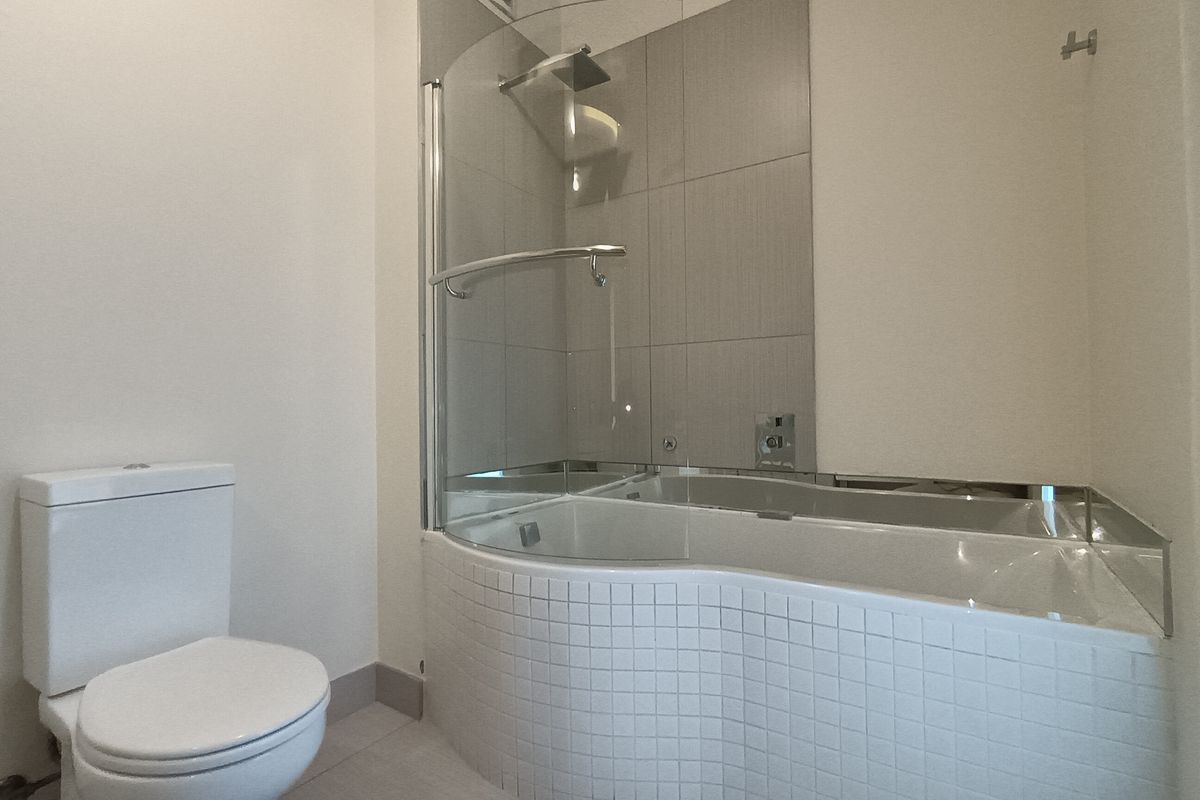 A modern bathroom featuring a curved shower-over-bath combination with glass screen, tiled splashback, and a standard white toilet.