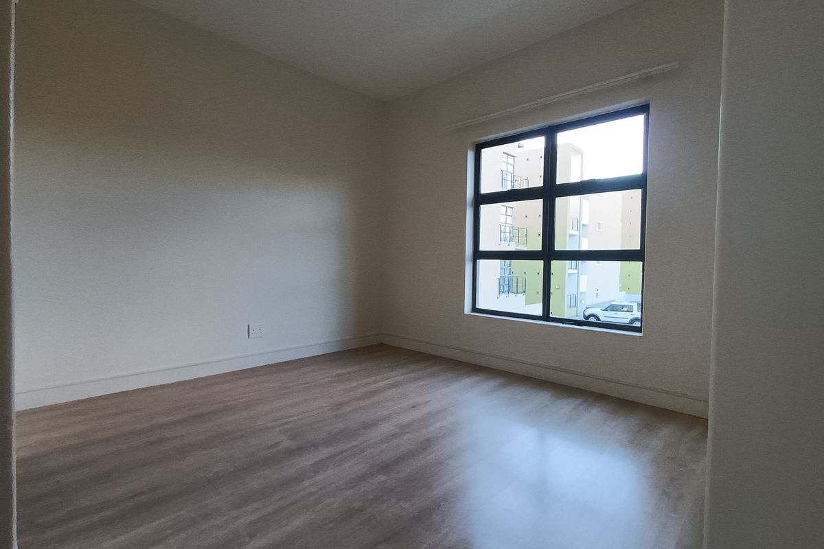 A bright, empty bedroom featuring neutral walls, wood-look laminate flooring, and a large window providing natural light.