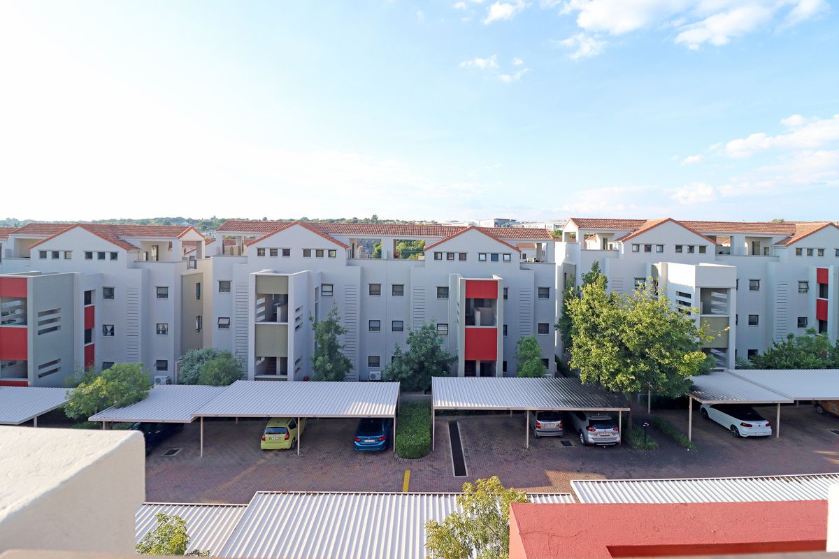 Elevated view of an apartment complex featuring multiple residential blocks, covered parking bays, and paved driveway areas.