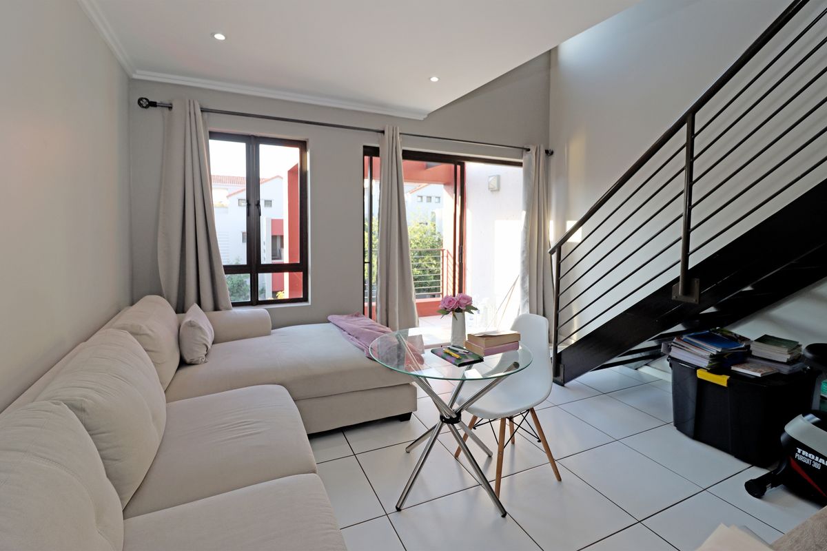 Bright living area featuring tiled flooring, recessed lighting, and a modern metal staircase, with direct access to an outdoor balcony through sliding glass doors.