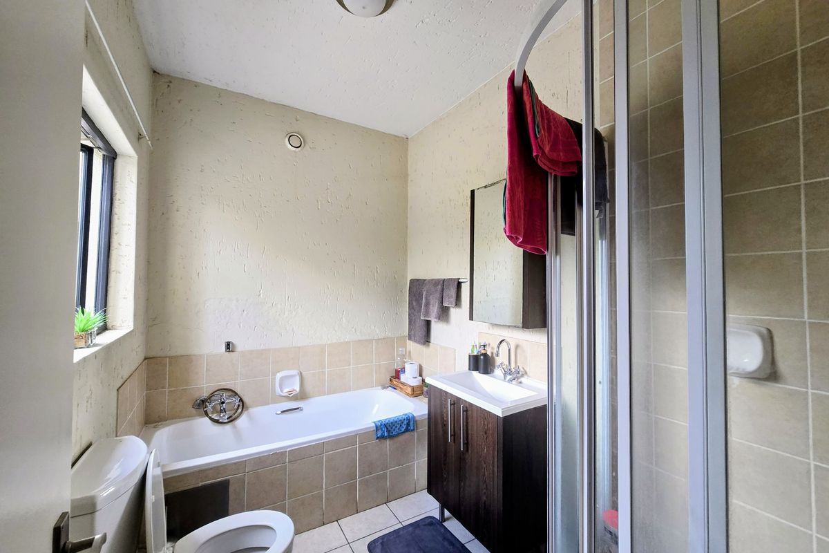 A functional bathroom featuring a built-in bathtub, separate shower enclosure, vanity cabinet with basin, and tiled flooring.