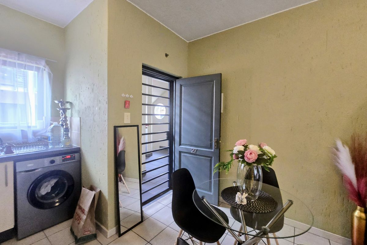 A compact kitchen area featuring tiled flooring, built-in cabinetry, and a dedicated space for a washing machine, leading to an exterior security gate.