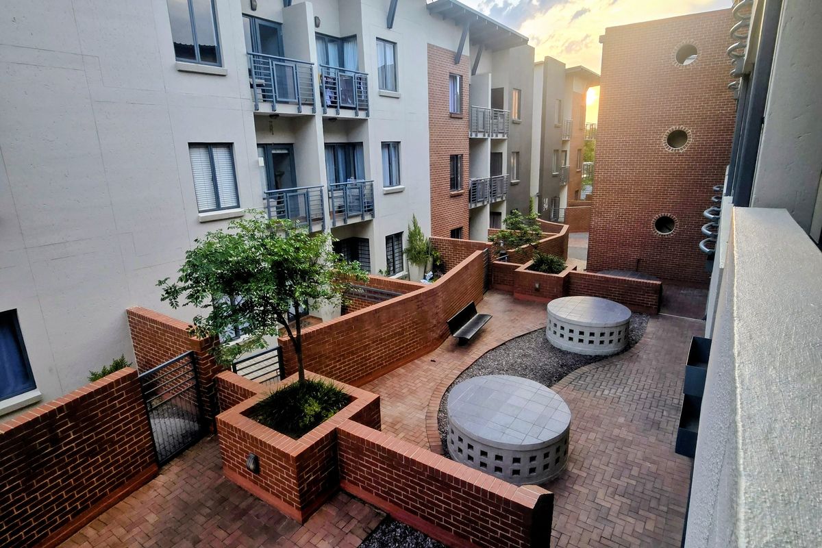 A well-maintained communal courtyard area featuring brick paving, tiered brick retaining walls, and integrated circular seating between apartment building wings.