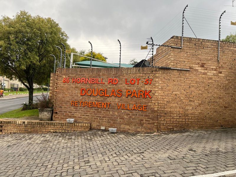 Entrance signage and perimeter brick walling for Douglas Park Retirement Village, featuring security fencing and paved driveway access.
