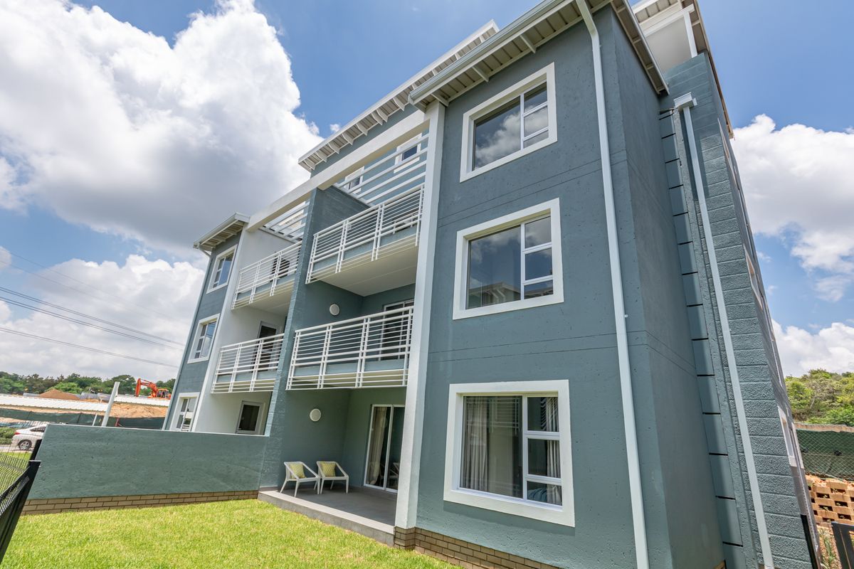 A modern multi-story apartment building exterior featuring private balconies, sliding glass doors, and a well-maintained lawn area.
