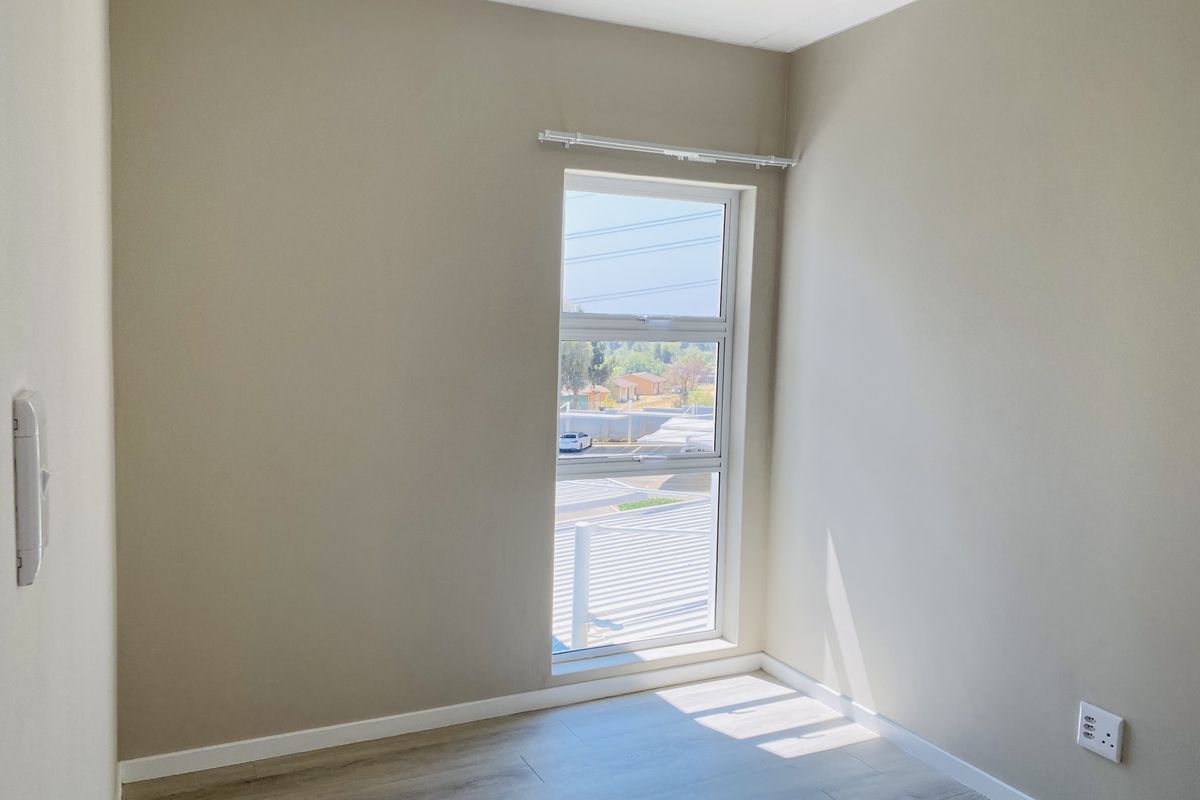 A bright, empty bedroom featuring modern laminate flooring, neutral wall tones, and a large window with a fitted curtain rail.