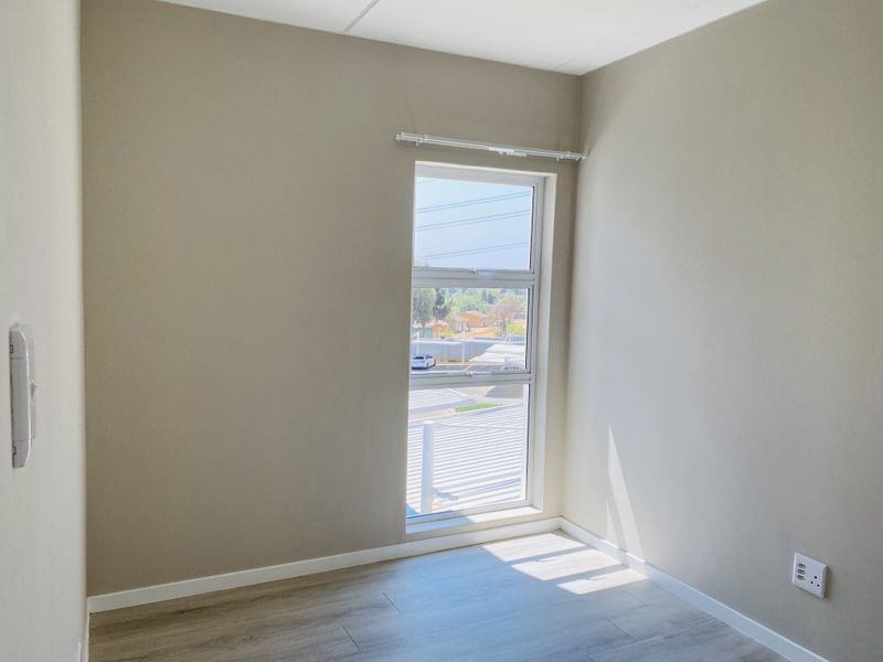 A bright, empty bedroom featuring modern laminate flooring, neutral wall tones, and a large window with a fitted curtain rail.
