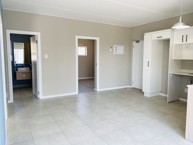 An open-plan living and kitchen area featuring neutral wall tones, tiled flooring, and built-in cabinetry, providing a clean and versatile space.