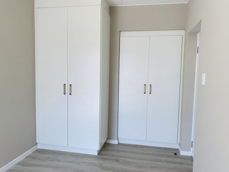 A clean, bright bedroom featuring modern white built-in cupboards and neutral laminate flooring, offering a versatile space ready for personalization.