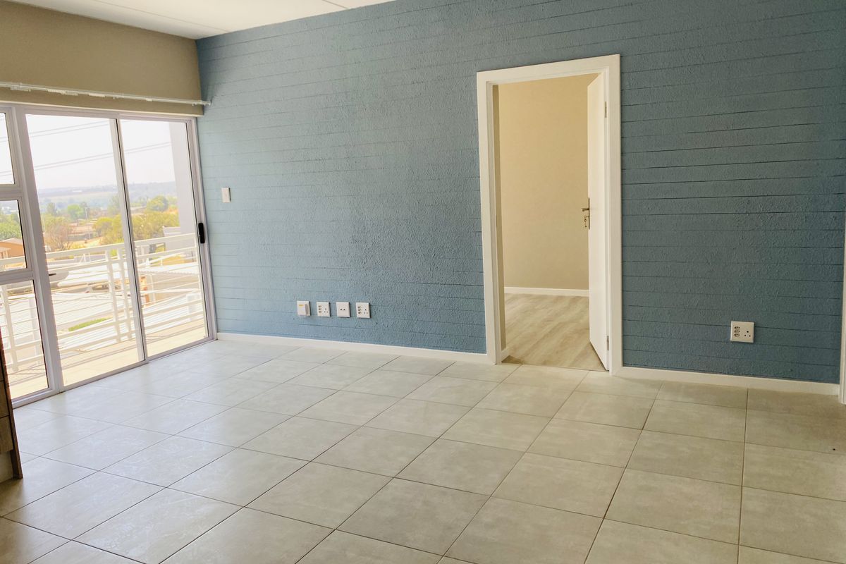 An empty living room featuring tiled flooring, a textured blue accent wall, and a sliding glass door leading to a balcony.