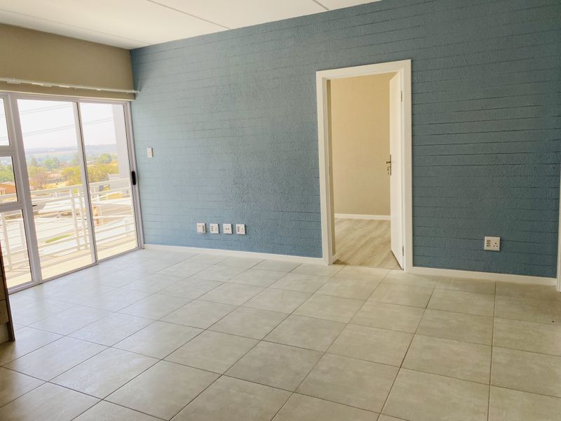 An empty living room featuring tiled flooring, a textured blue accent wall, and a sliding glass door leading to a balcony.