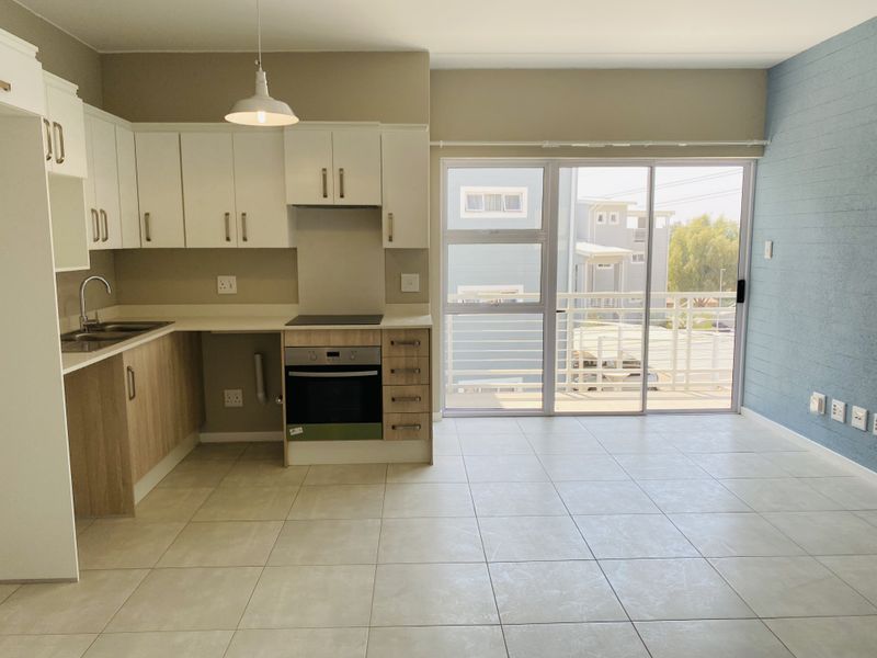 Modern open-plan kitchen and living area featuring tiled floors, built-in cabinetry, integrated appliances, and direct access to a private balcony through sliding glass doors.