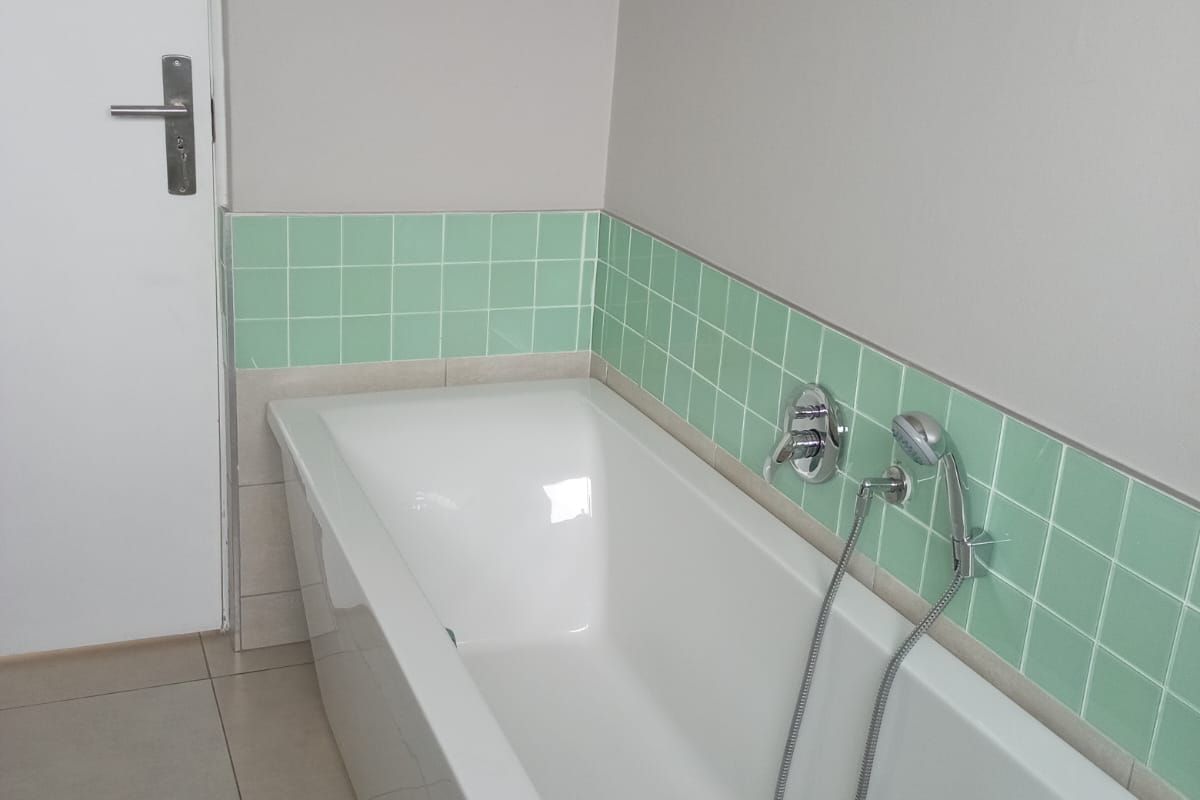 A clean, functional bathroom featuring a white bathtub with a shower mixer and mint green tiled splashback.
