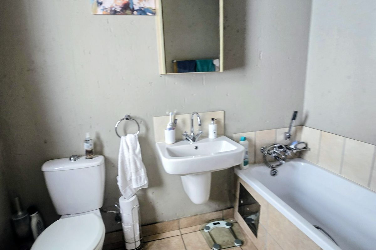 A functional bathroom featuring a white pedestal basin, a standard toilet, and a bathtub with tiled surround and wall-mounted mirror cabinet.