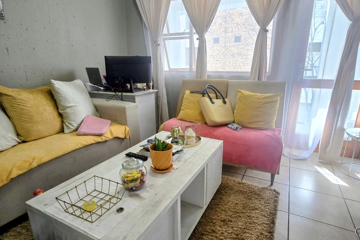 A living room area featuring tiled flooring and large windows with curtains, providing natural light and access to the exterior.