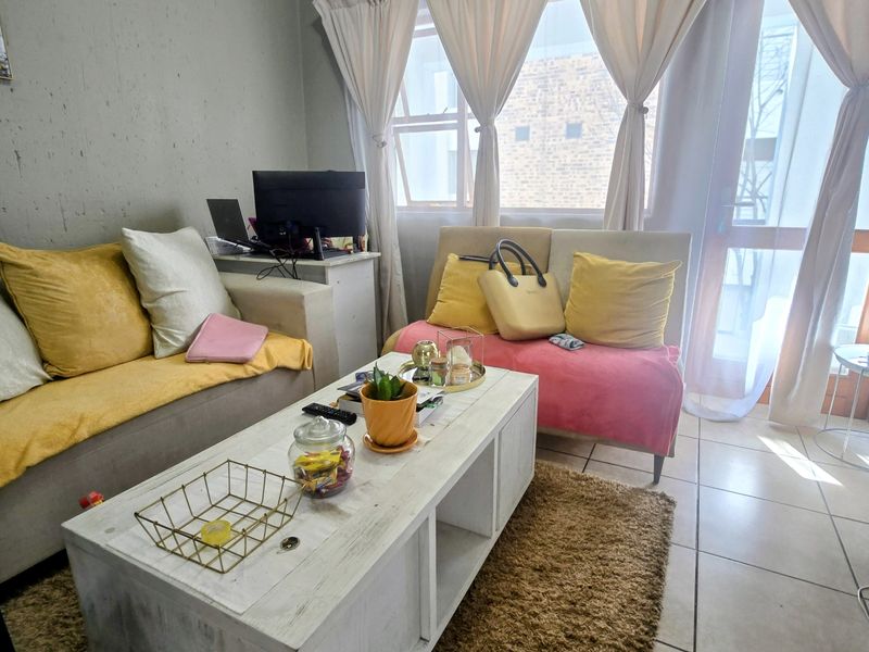A living room area featuring tiled flooring and large windows with curtains, providing natural light and access to the exterior.