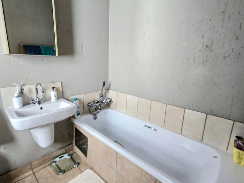 A functional bathroom featuring a wall-mounted basin, a standard bathtub with tiled surround, and a wall-mounted mirror.