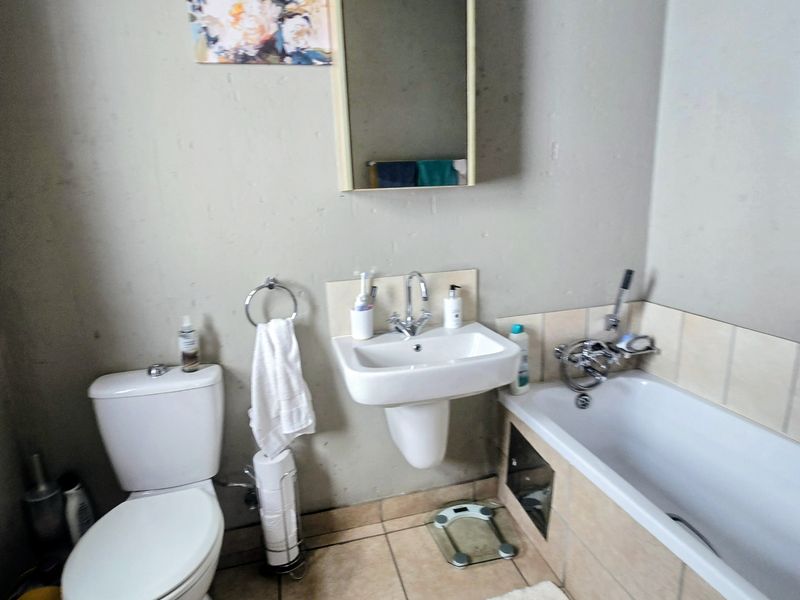A functional bathroom featuring a white pedestal basin, a standard toilet, and a bathtub with tiled surround and wall-mounted mirror cabinet.