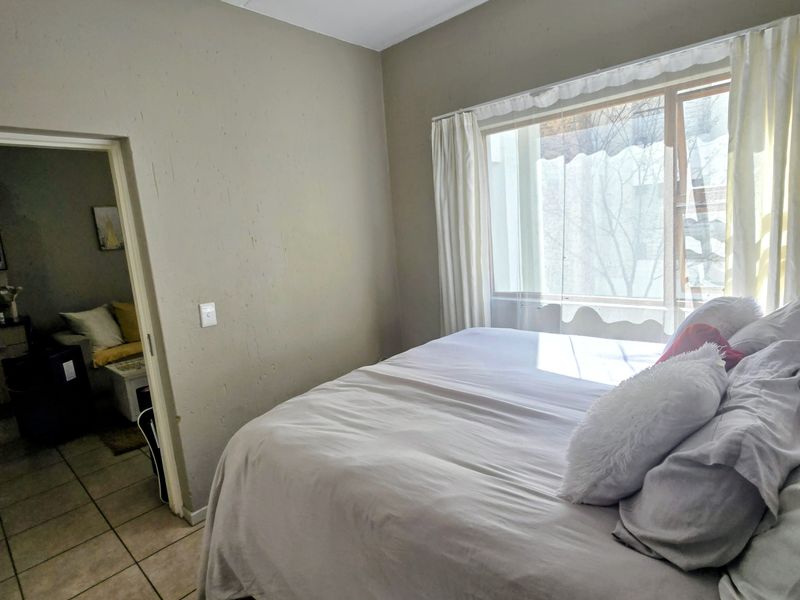 A bedroom featuring tiled flooring, a large window allowing natural light, and direct access to an adjacent living space.