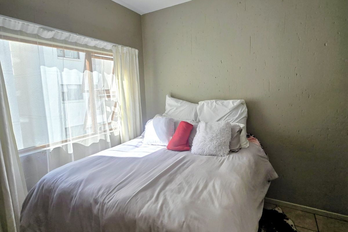 A bedroom featuring tiled flooring, a large window with natural light, and a central ceiling light fixture.