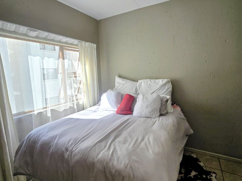 A bedroom featuring tiled flooring, a large window with natural light, and a central ceiling light fixture.