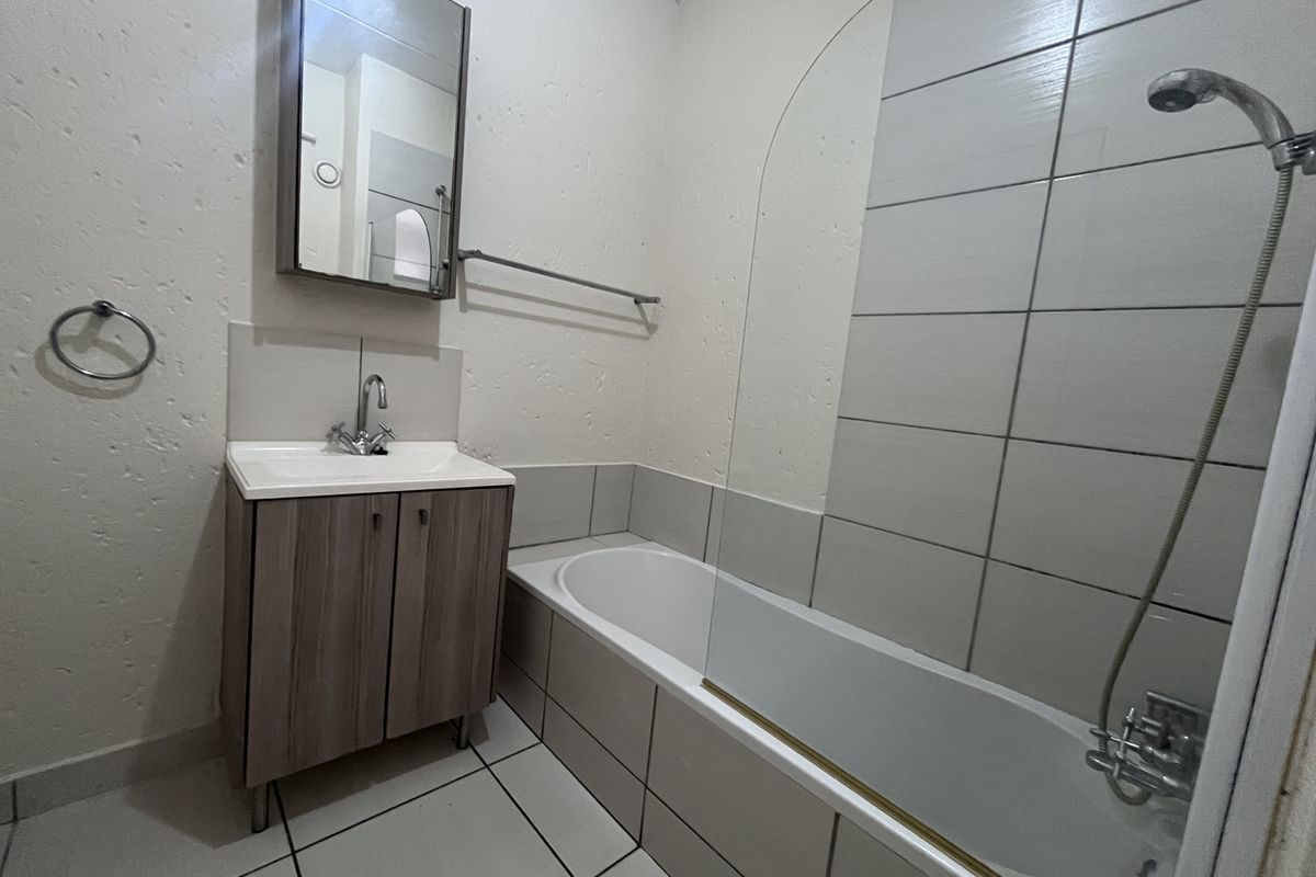 A functional bathroom featuring a built-in vanity, a bathtub with a shower mixer, and a glass shower screen.