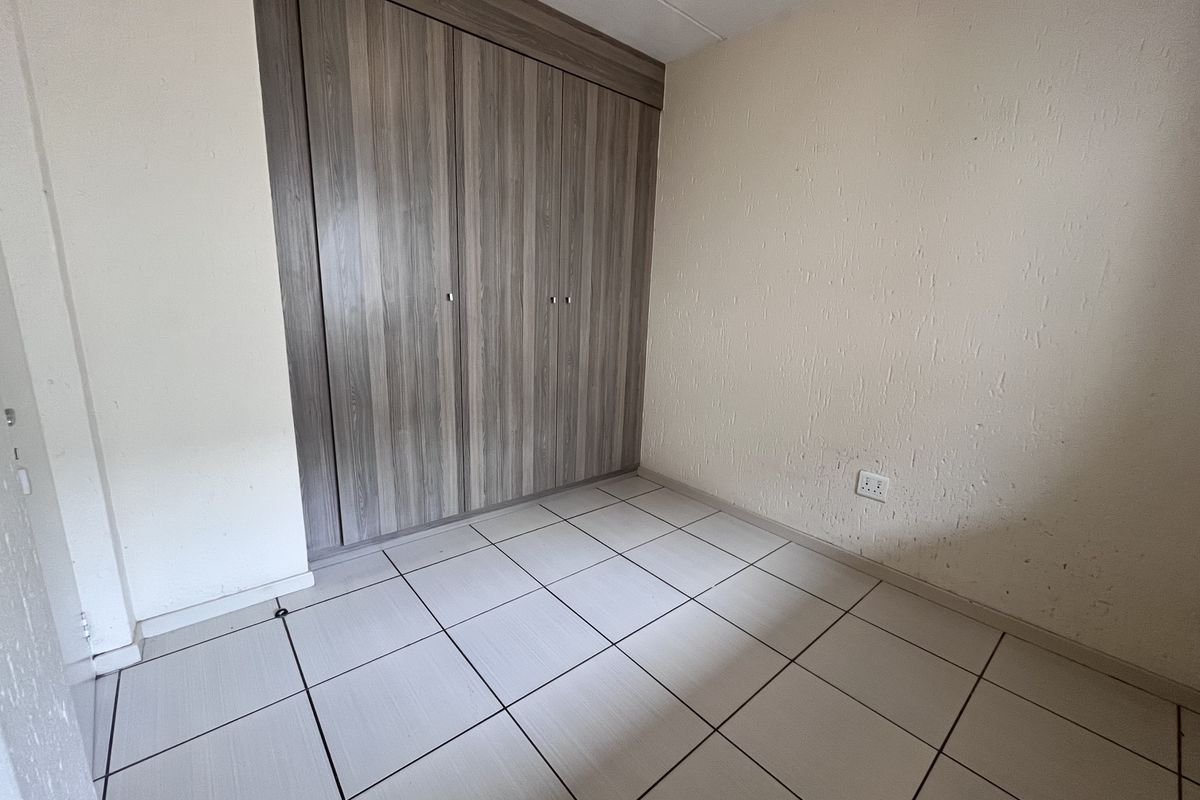 A compact bedroom featuring neutral tiled flooring and built-in wooden cabinetry with ample storage space.