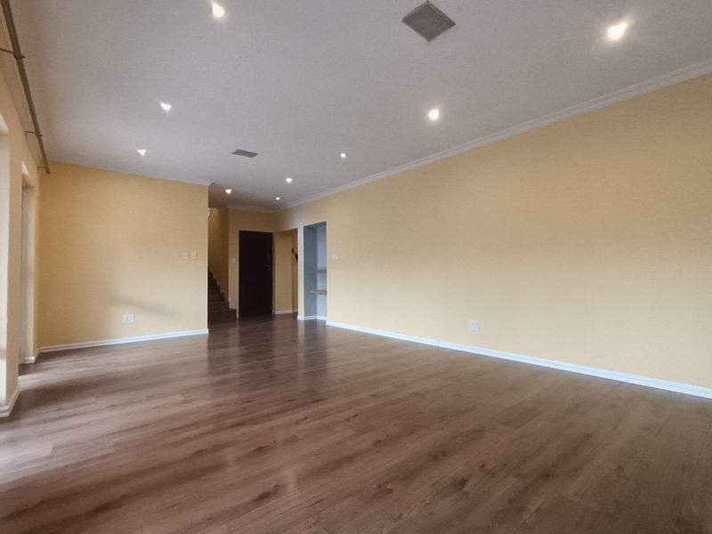 Spacious, empty living area featuring modern laminate flooring, recessed downlighting, and a neutral color palette, providing a versatile blank canvas for interior design.