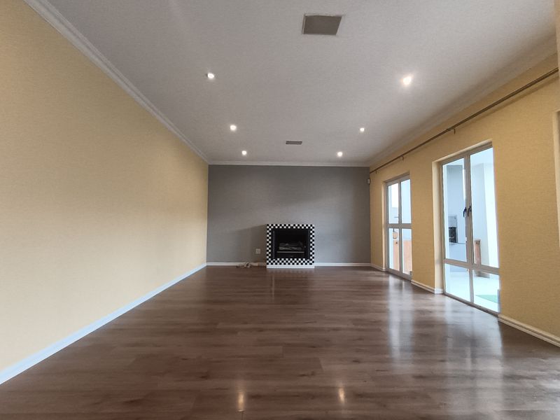 Spacious living room featuring laminate flooring, recessed downlights, a built-in fireplace with a decorative surround, and large sliding glass doors providing natural light.