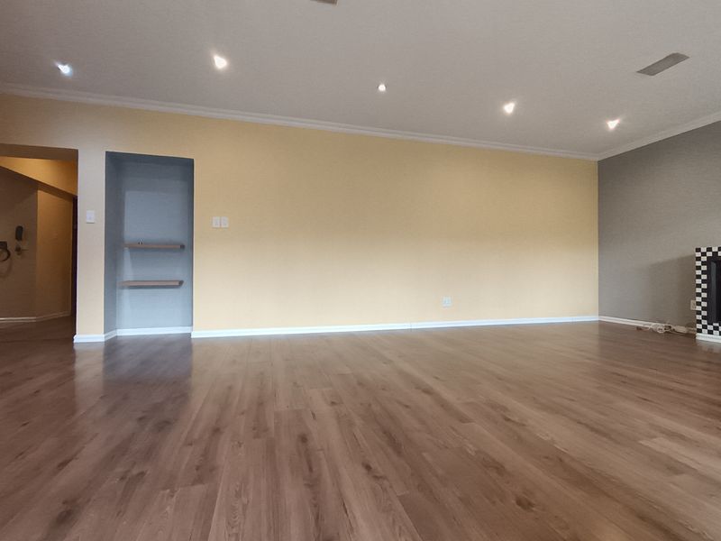 Spacious living area featuring laminate flooring, recessed downlights, a built-in fireplace with checkered tile detail, and a convenient recessed shelving nook.