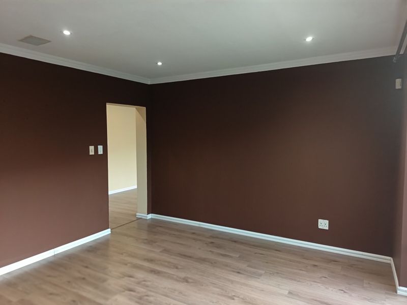 An empty living room featuring laminate flooring, recessed downlights, and dark brown painted walls with white trim.