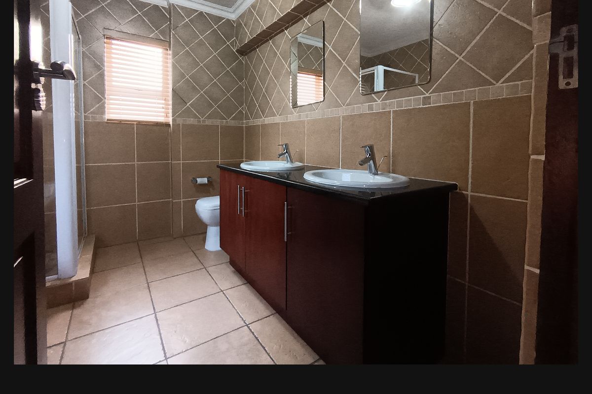 A functional bathroom featuring a double vanity with dual basins, a shower enclosure, and tiled finishes throughout.