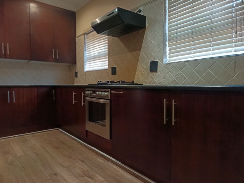 A functional kitchen featuring dark wood cabinetry, granite countertops, a built-in oven with gas hob, and a tiled backsplash.
