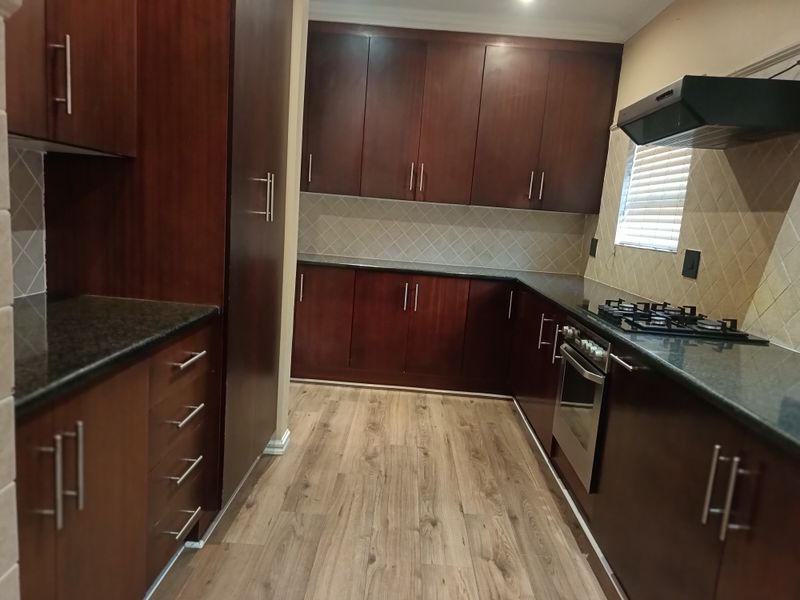 A well-maintained kitchen featuring dark wood cabinetry, granite countertops, built-in oven, gas hob, and a tiled backsplash with modern laminate flooring.