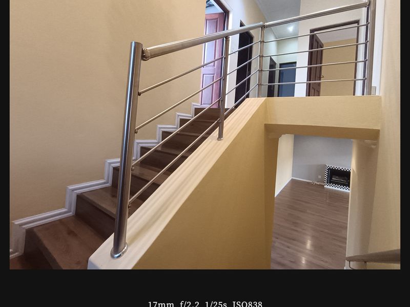 A bright hallway featuring a modern stainless steel balustrade, wooden staircase, and laminate flooring, overlooking a lower level living area with a built-in fireplace.
